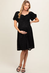woman wearing a black lace maternity dress with short puff sleeves and a baby bump visible