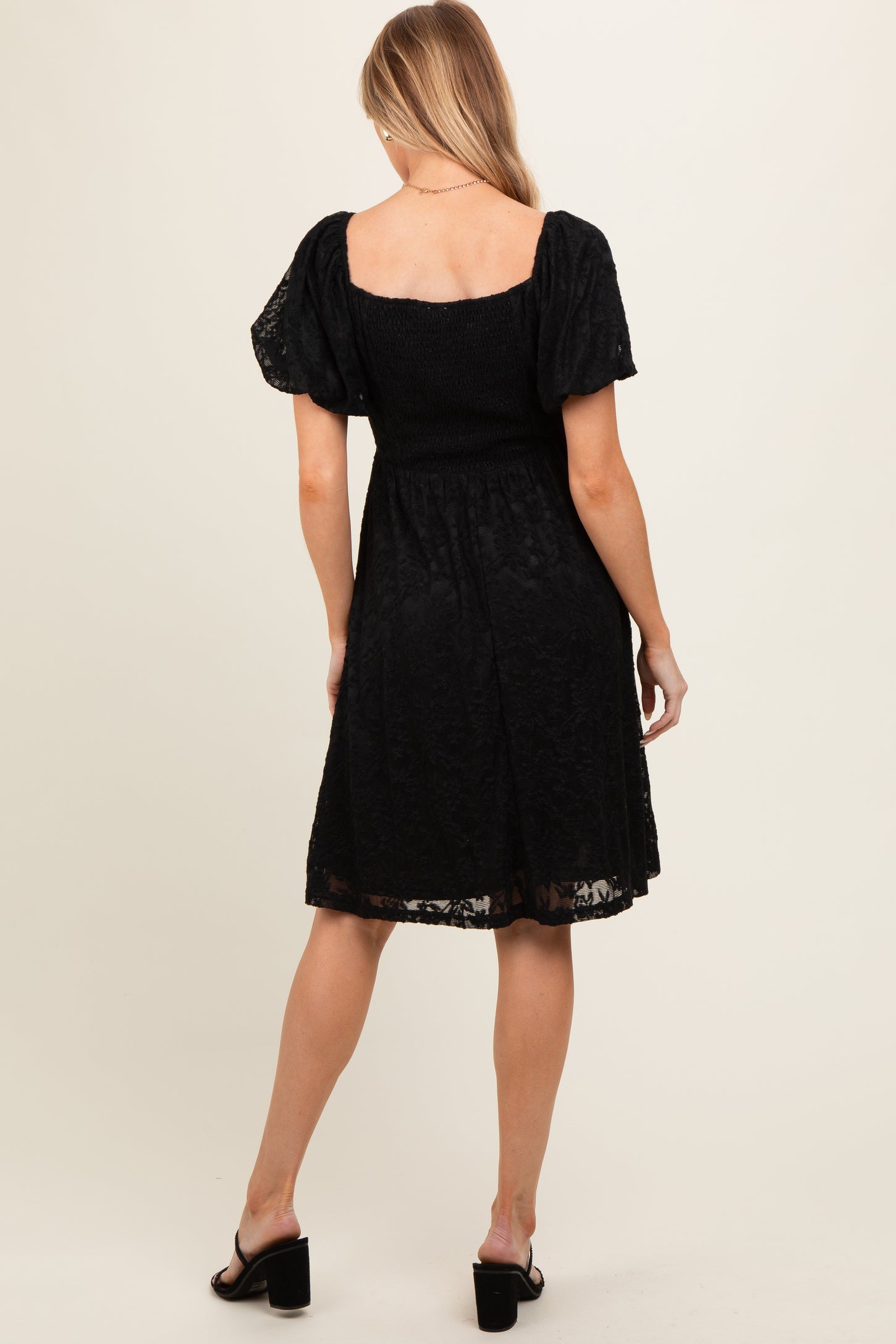 woman wearing a black lace maternity dress with a square neckline and puff sleeves, showing the back view