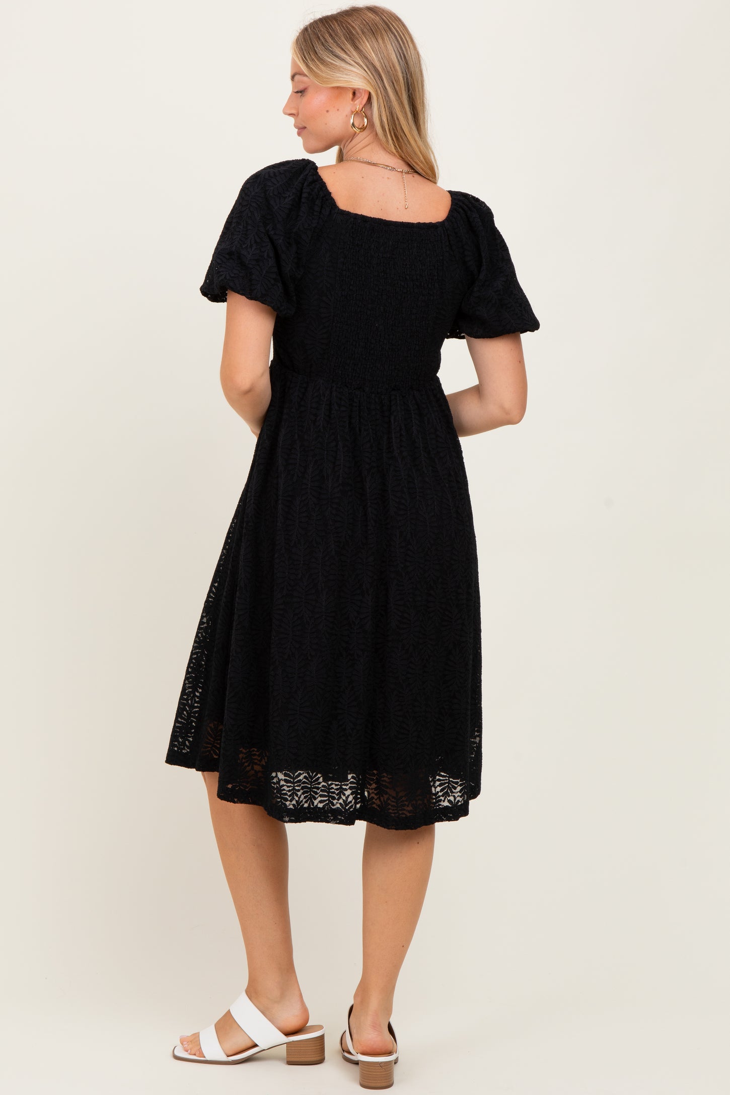 woman wearing a black short sleeve dress with a square neckline and a flowy skirt, viewed from the back