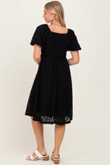 woman wearing a black short sleeve dress with a square neckline and a flowy skirt, viewed from the back