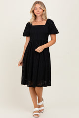 woman wearing a black short sleeve lace dress with a square neckline and a flared skirt