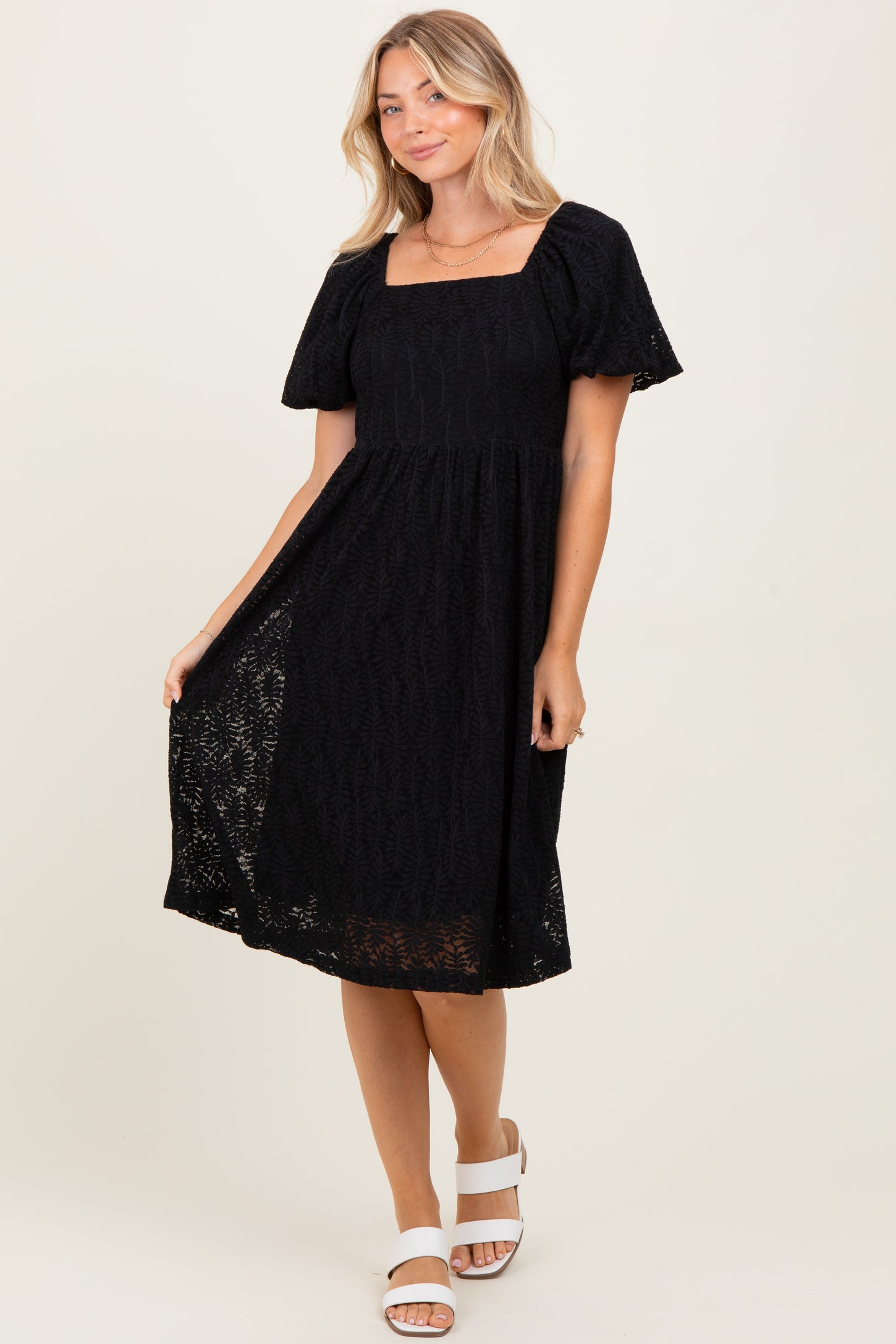 woman wearing a black short sleeve square neck midi dress with a lace overlay and a-flowy skirt