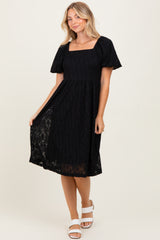 woman wearing a black short sleeve square neck midi dress with a lace overlay and a-flowy skirt