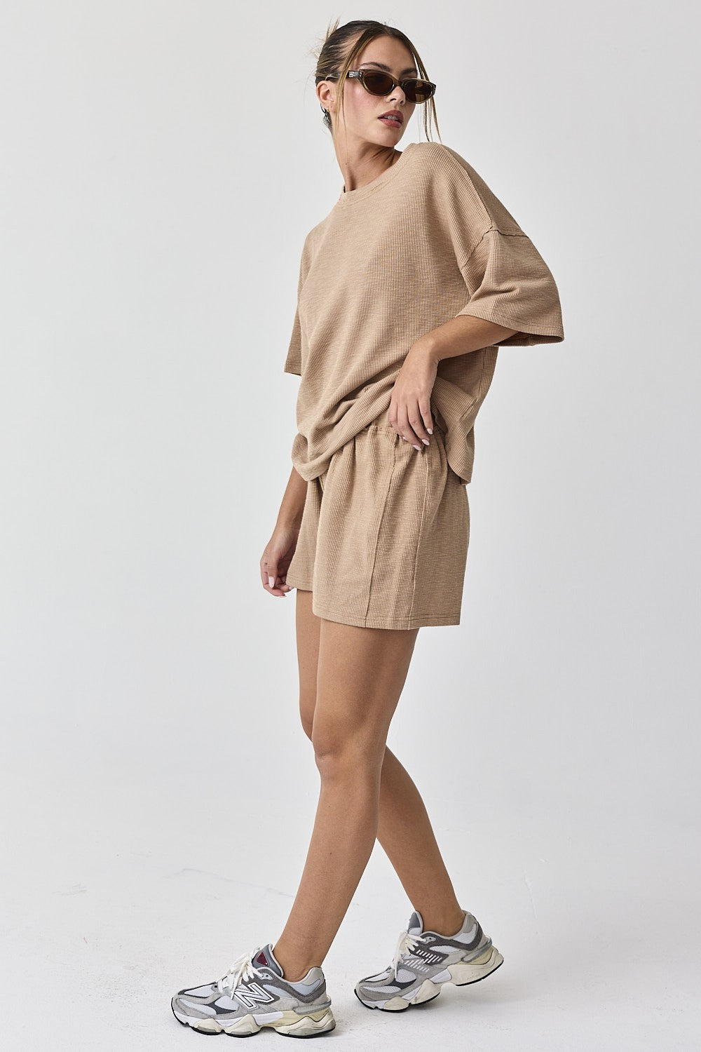 woman wearing a beige oversized waffle knit t-shirt and matching shorts, paired with sporty sneakers and sunglasses