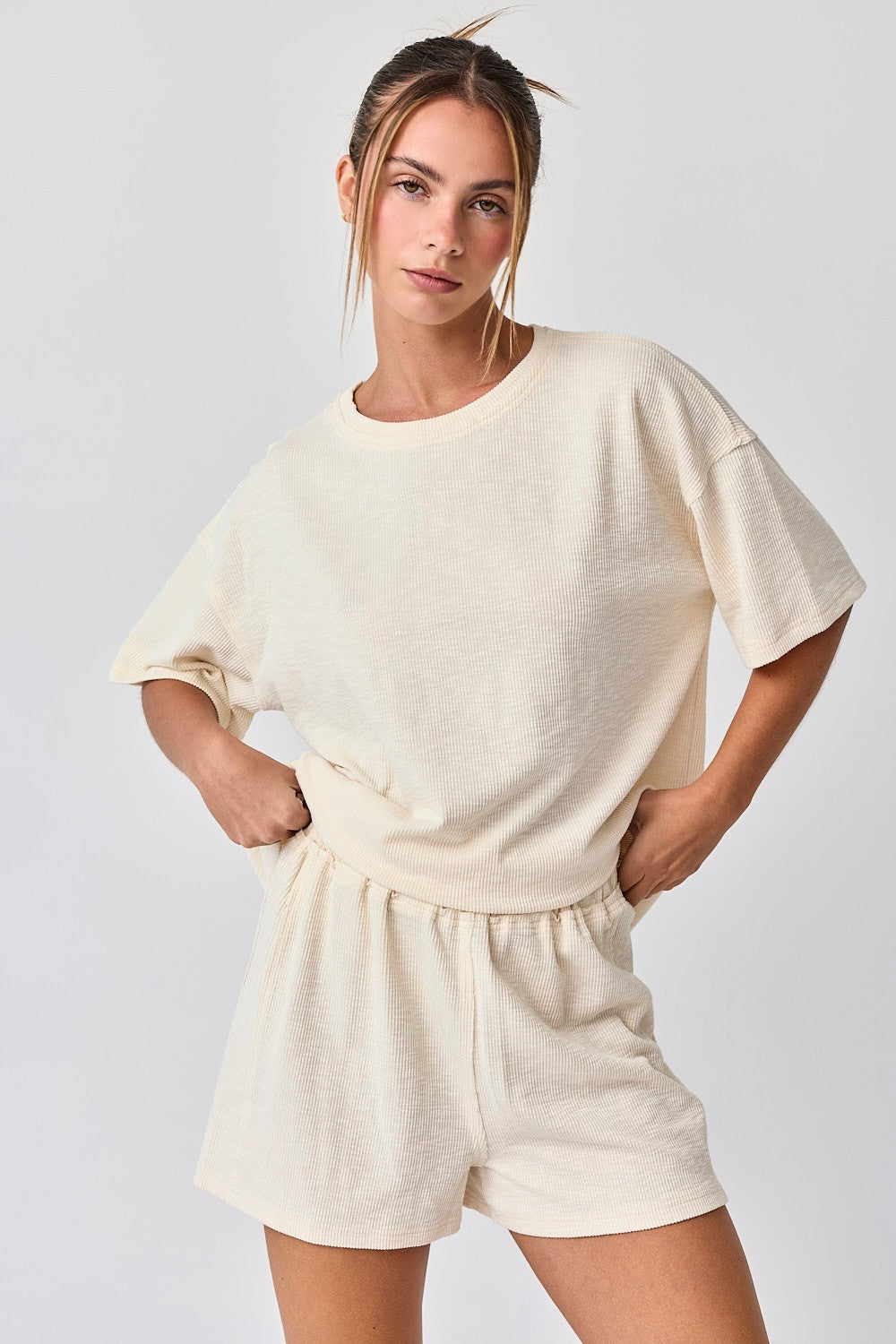 woman wearing a beige textured short sleeve top and matching shorts, standing with hands on her hips