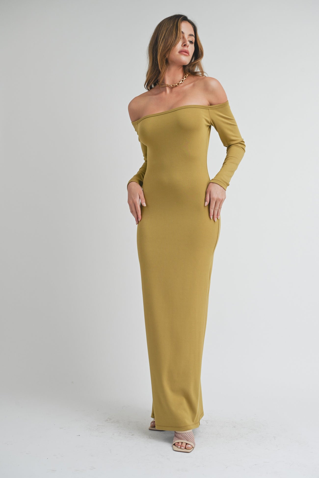woman wearing a long olive green off-shoulder maxi dress with fitted silhouette and strappy heels