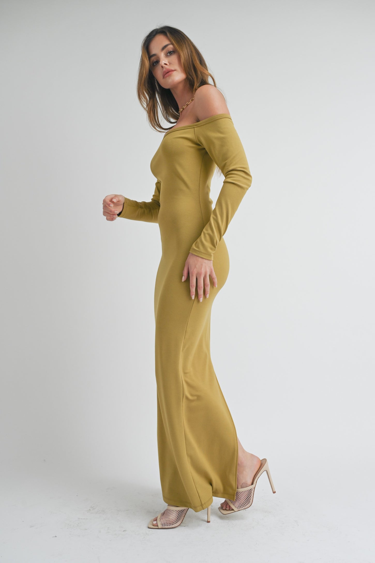 woman wearing a long-sleeve olive green off-the-shoulder maxi dress with side slits and high heels