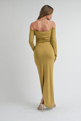 woman wearing an olive green off-shoulder maxi dress with a back slit, standing with her back to the camera
