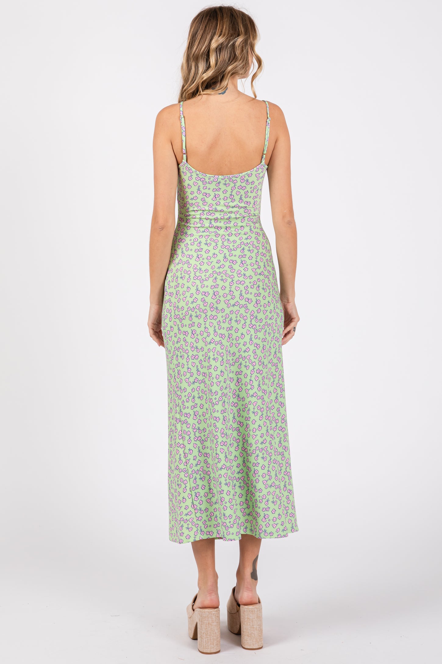 woman wearing a light green floral midi dress with adjustable straps and a fitted silhouette, showing the back view