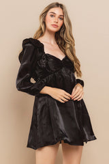 woman wearing a black satin mini dress with puff sleeves and a sweetheart neckline