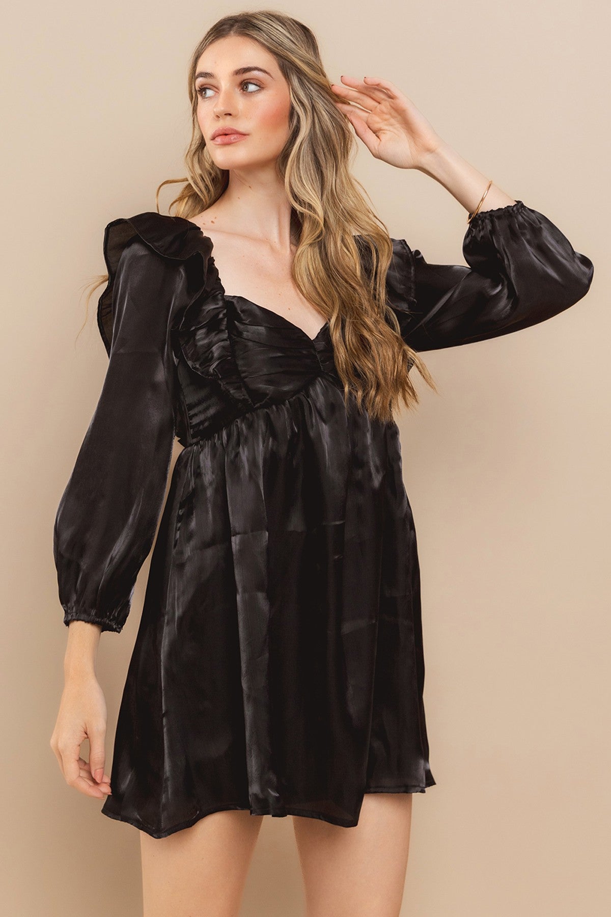woman wearing a black satin mini dress with puffed sleeves and a ruffled neckline, posing gracefully