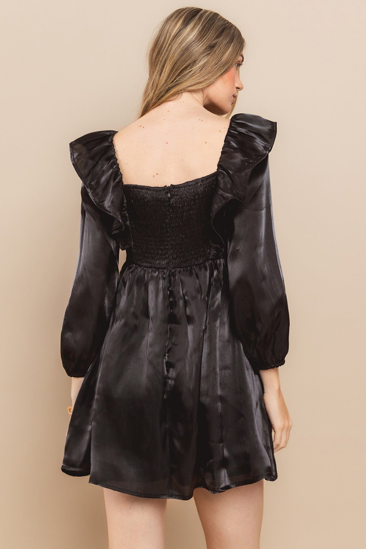 woman wearing a black satin dress with a smocked bodice and ruffled sleeves, showing the back view