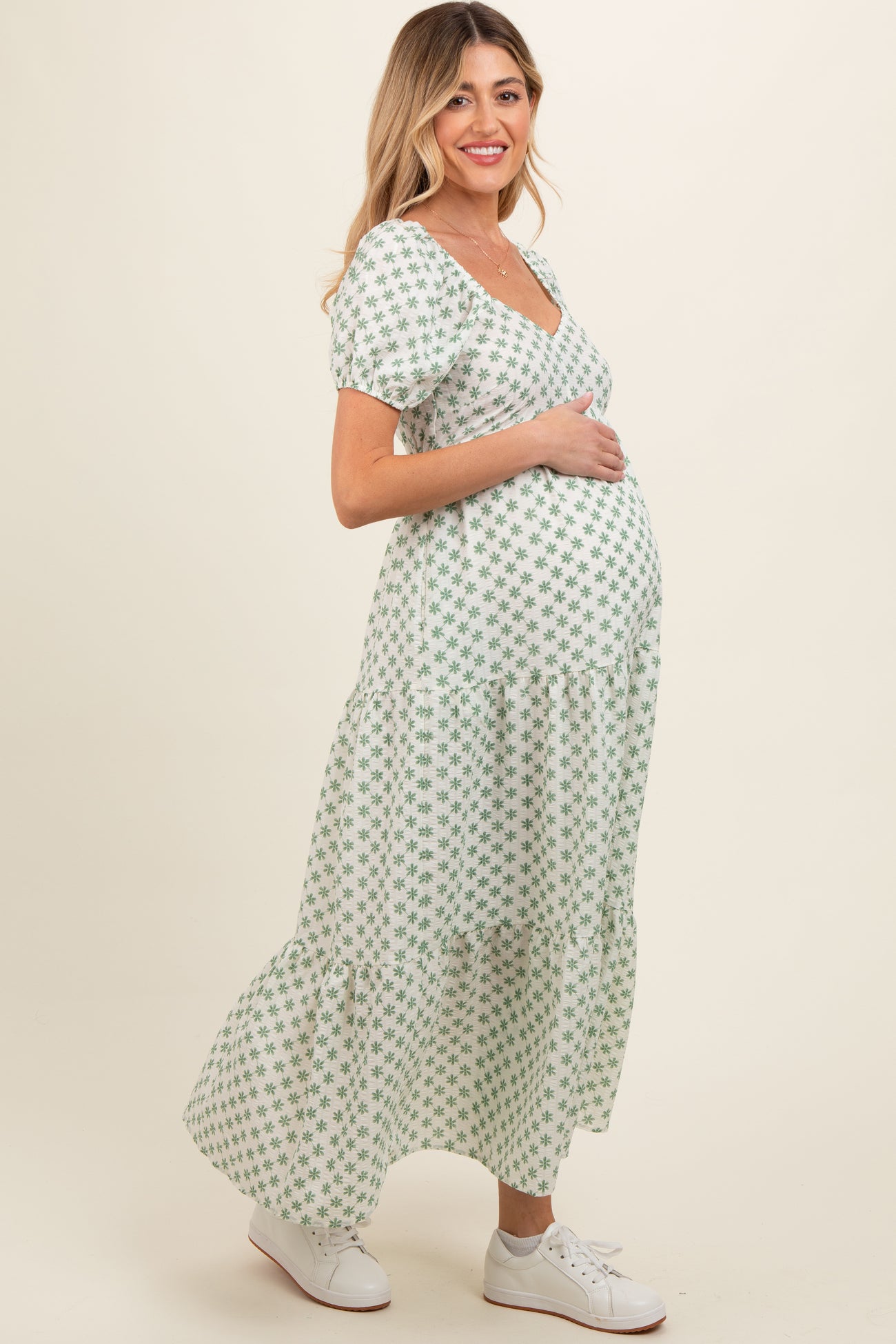 woman wearing a green floral maternity maxi dress while holding her baby bump