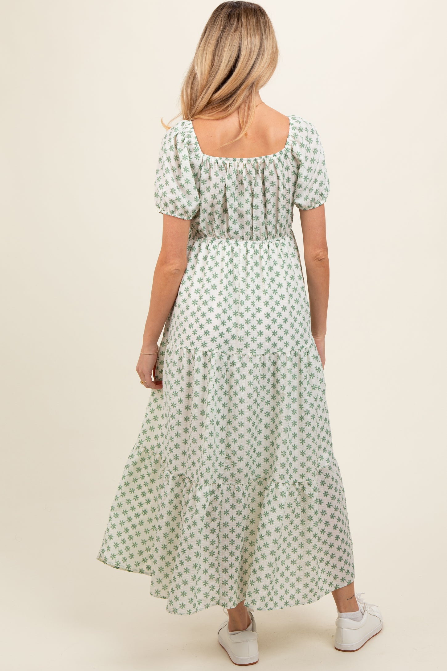 woman wearing a green floral print maternity maxi dress with puff sleeves and a tiered skirt, showing her baby bump