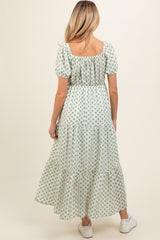 woman wearing a green floral print maternity maxi dress with puff sleeves and a tiered skirt, showing her baby bump