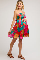 woman wearing a multi-colored floral maternity dress with a fitted bodice and flared skirt, holding her baby bump
