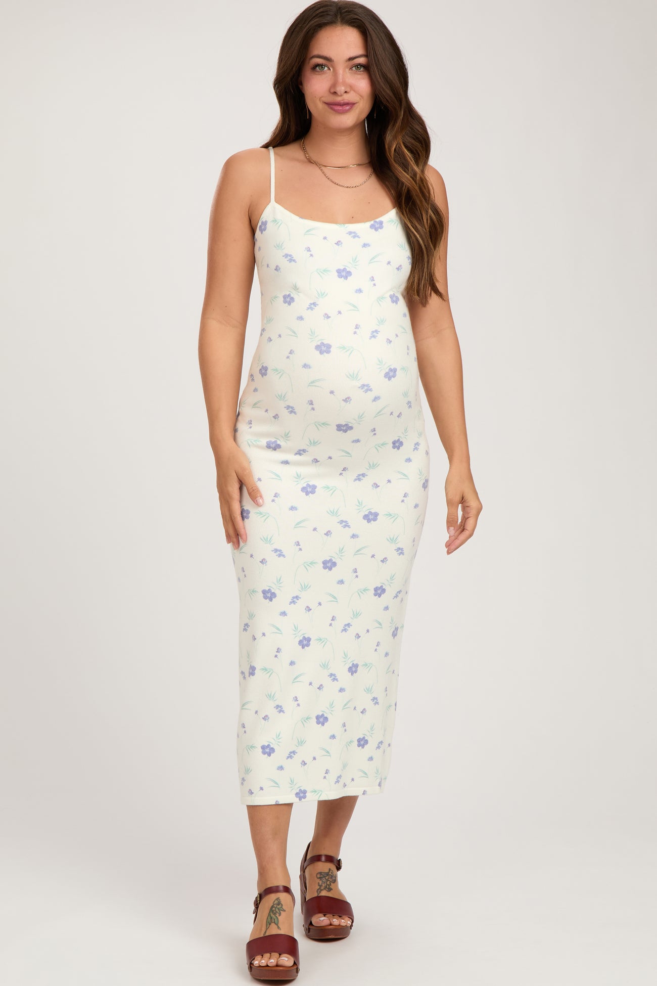 woman wearing a light green floral maternity dress with spaghetti straps and a visible baby bump