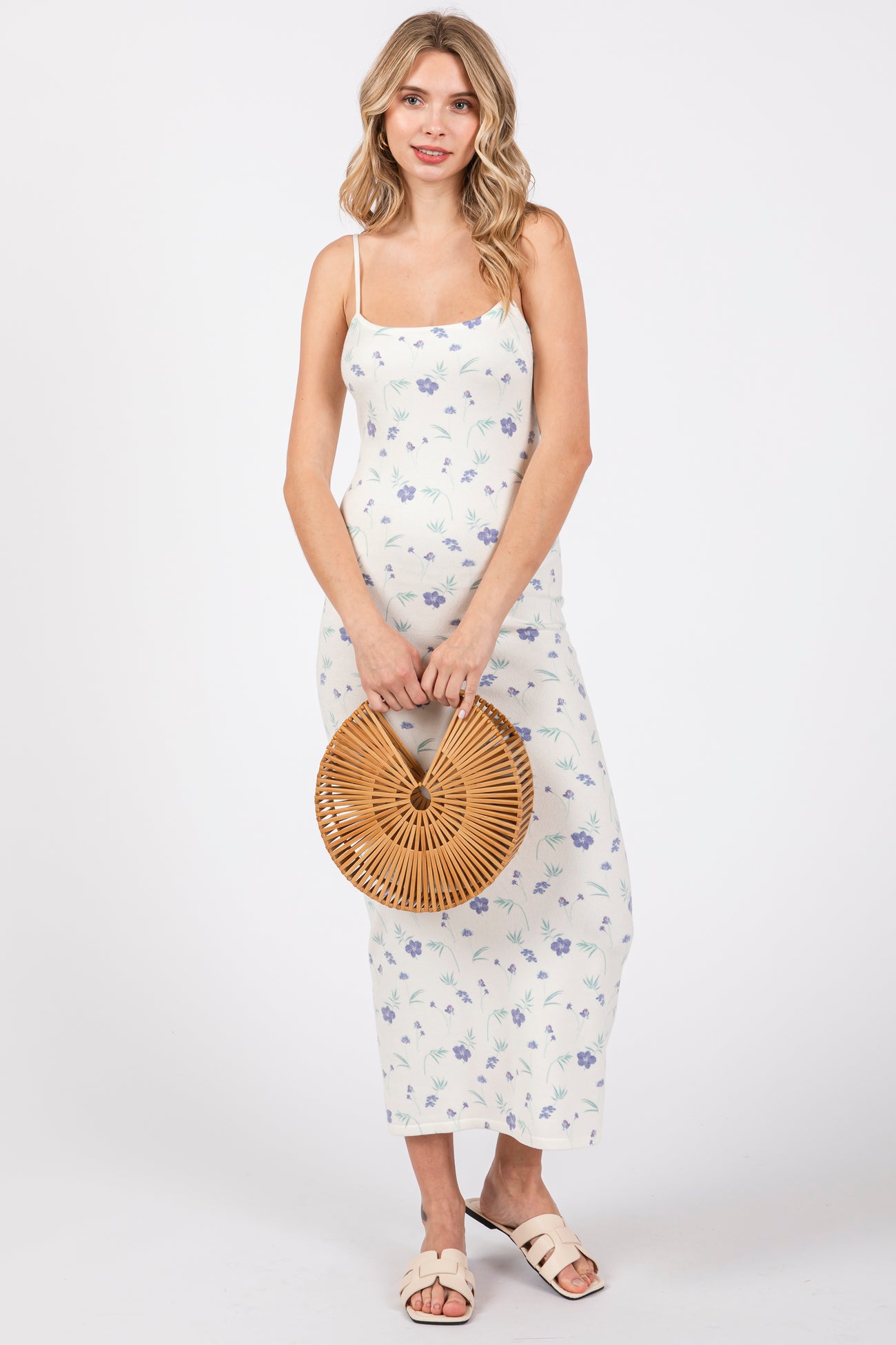 woman wearing a white floral maxi dress with thin straps and holding a round bamboo handbag