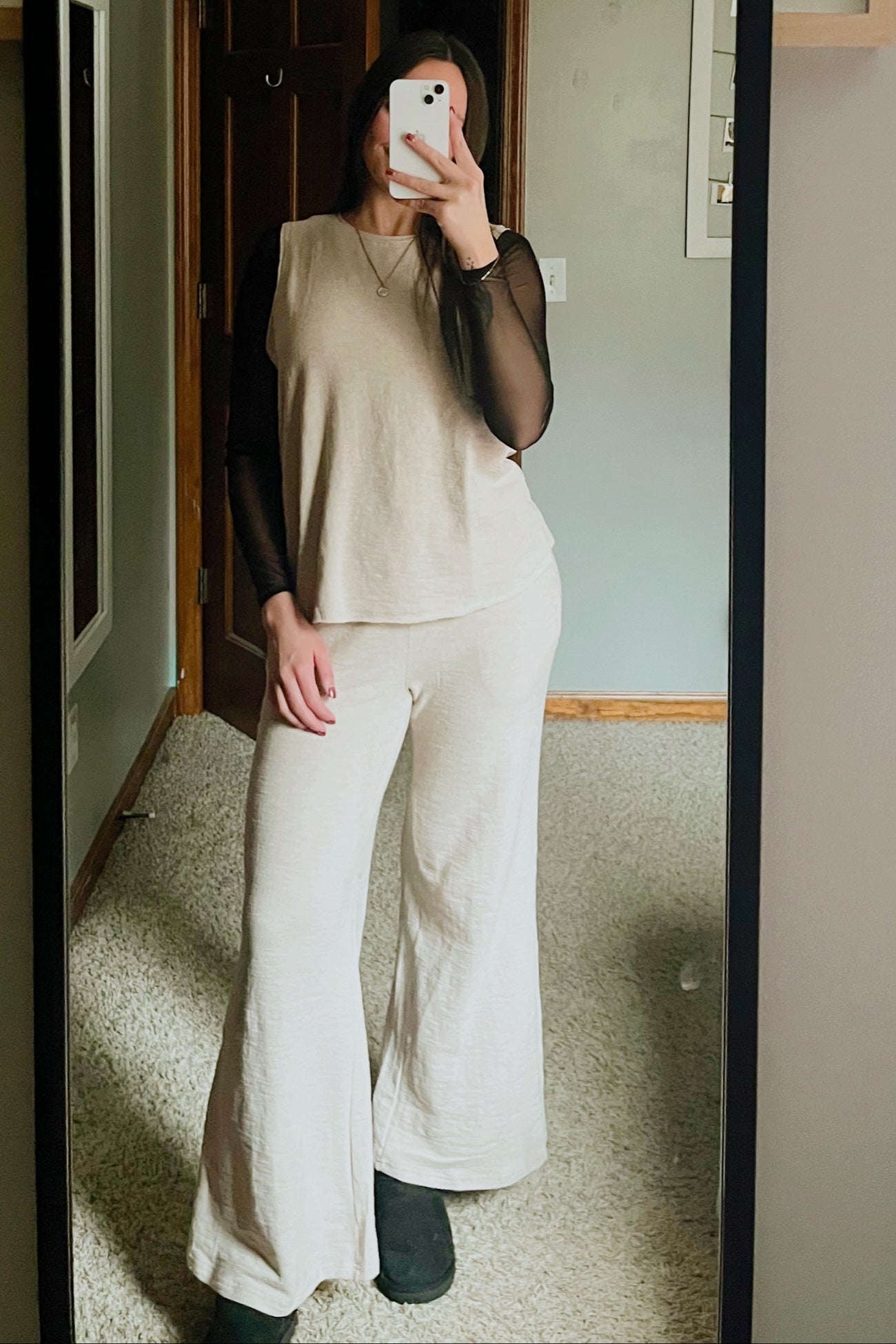 woman wearing a beige two-piece outfit consisting of a flowy top and wide-leg pants, with a black long-sleeve mesh layer underneath