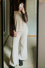 woman wearing a beige two-piece outfit consisting of a flowy top and wide-leg pants, with a black long-sleeve mesh layer underneath
