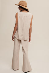 woman wearing a light beige sleeveless top and matching flared pants, with a hat and seen from the back