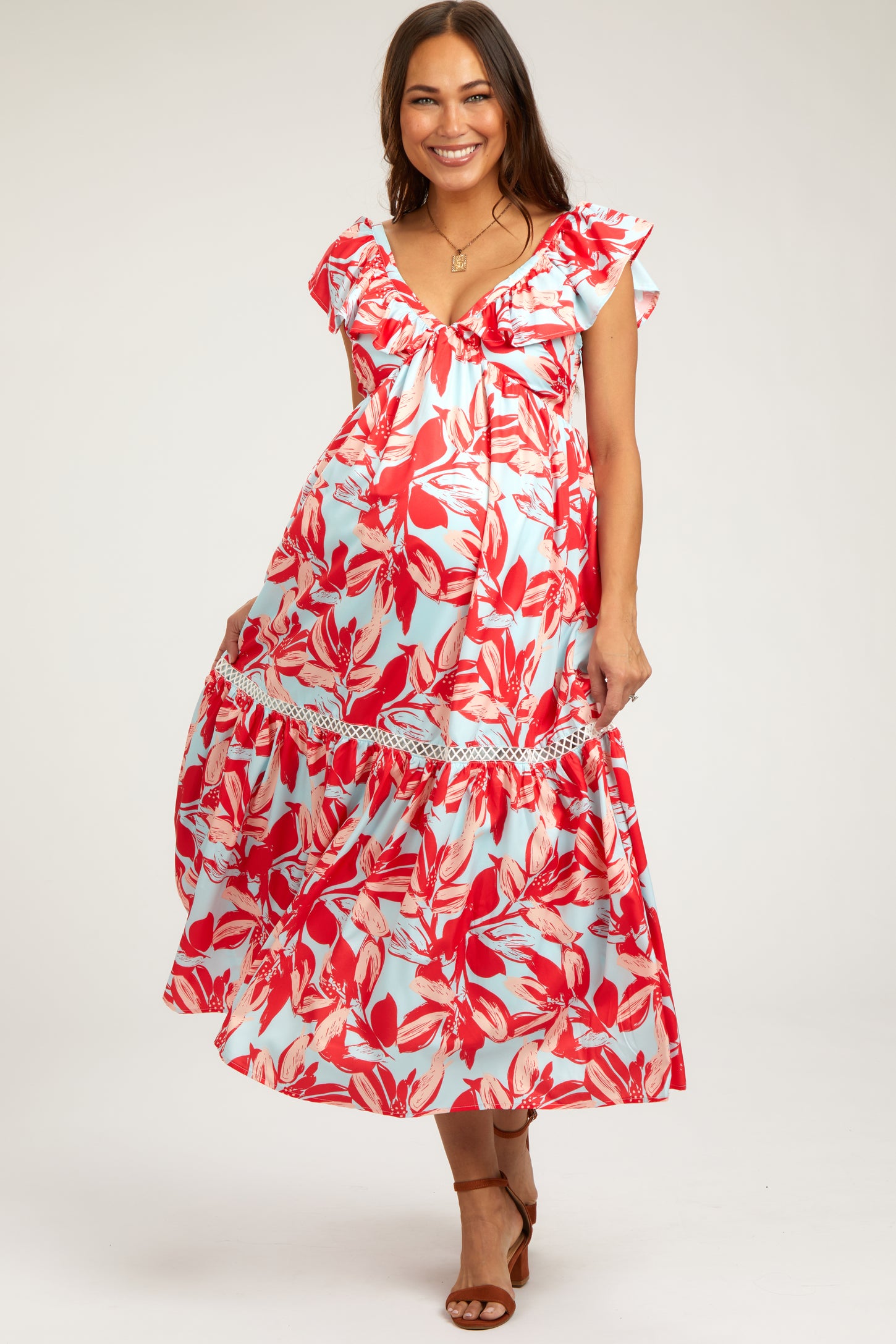 woman wearing a red and light blue floral maternity maxi dress with ruffled sleeves and a tiered hem, showcasing her baby bump