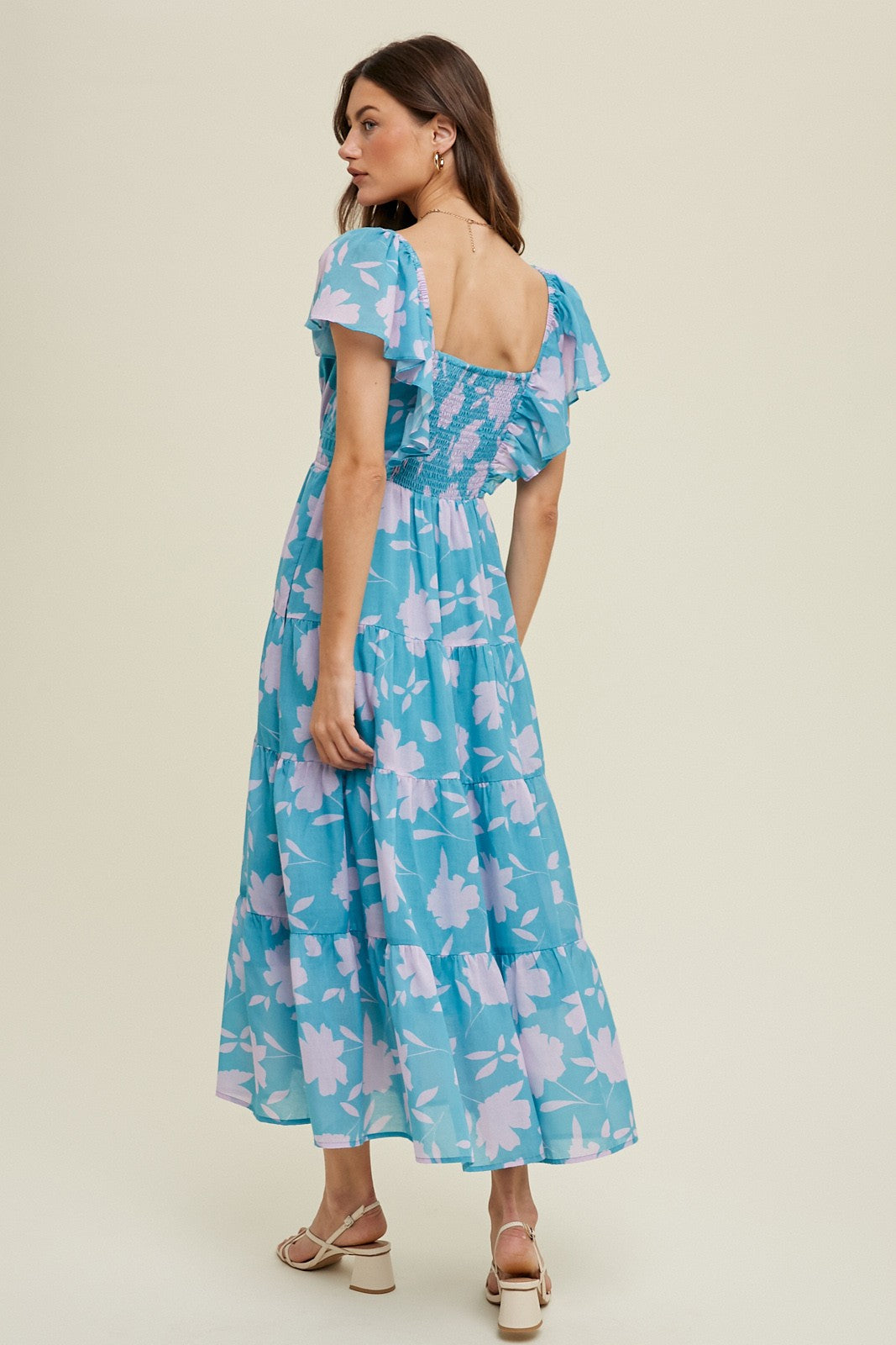 woman wearing a blue floral maxi dress with puff sleeves and a smocked bodice, standing with her back to the camera