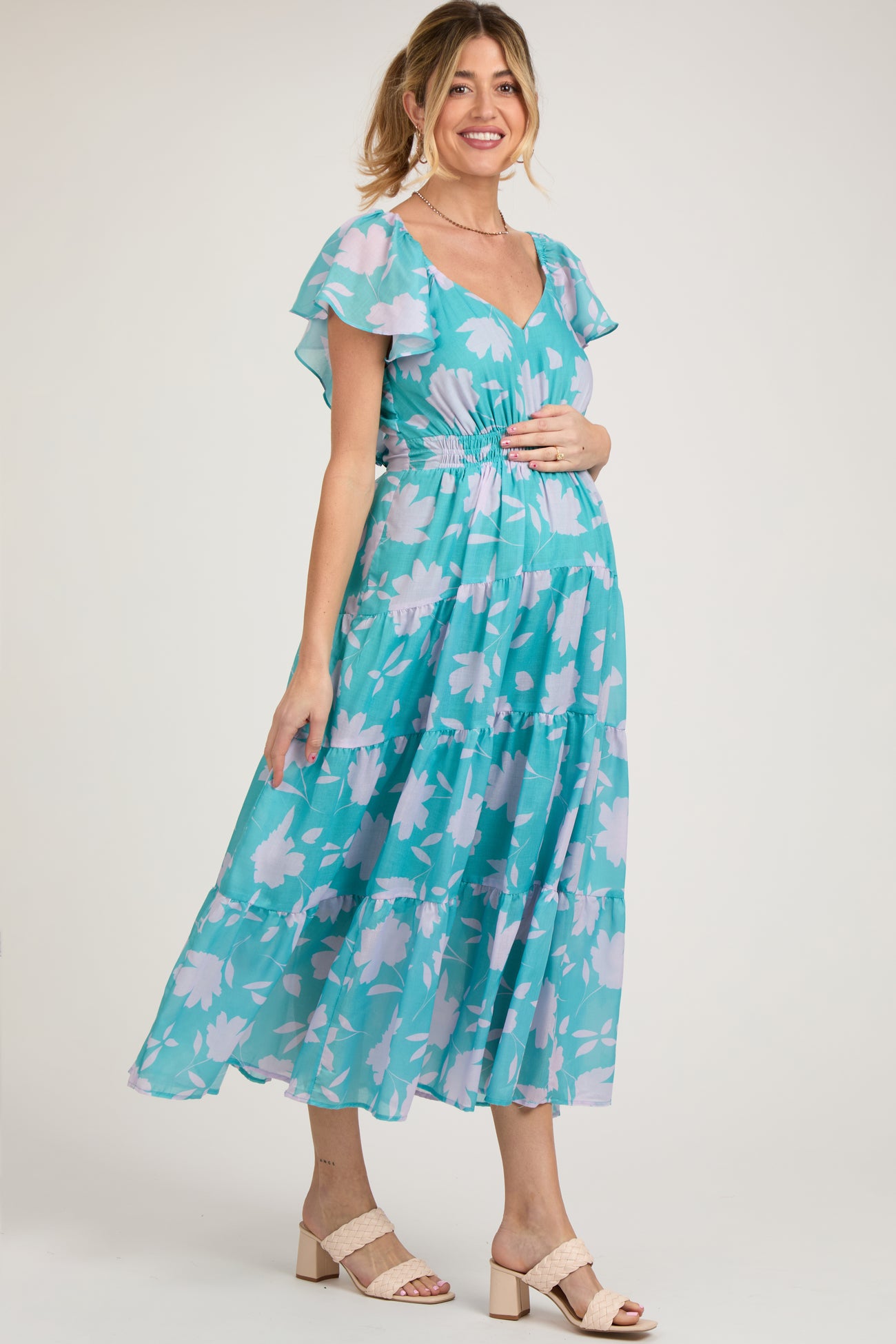 woman wearing a teal floral maternity maxi dress with a flattering v-neck and ruffled sleeves, showing her baby bump
