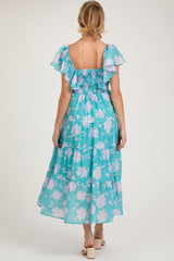 woman wearing a turquoise floral maternity dress with flutter sleeves and a tiered skirt, showing a baby bump