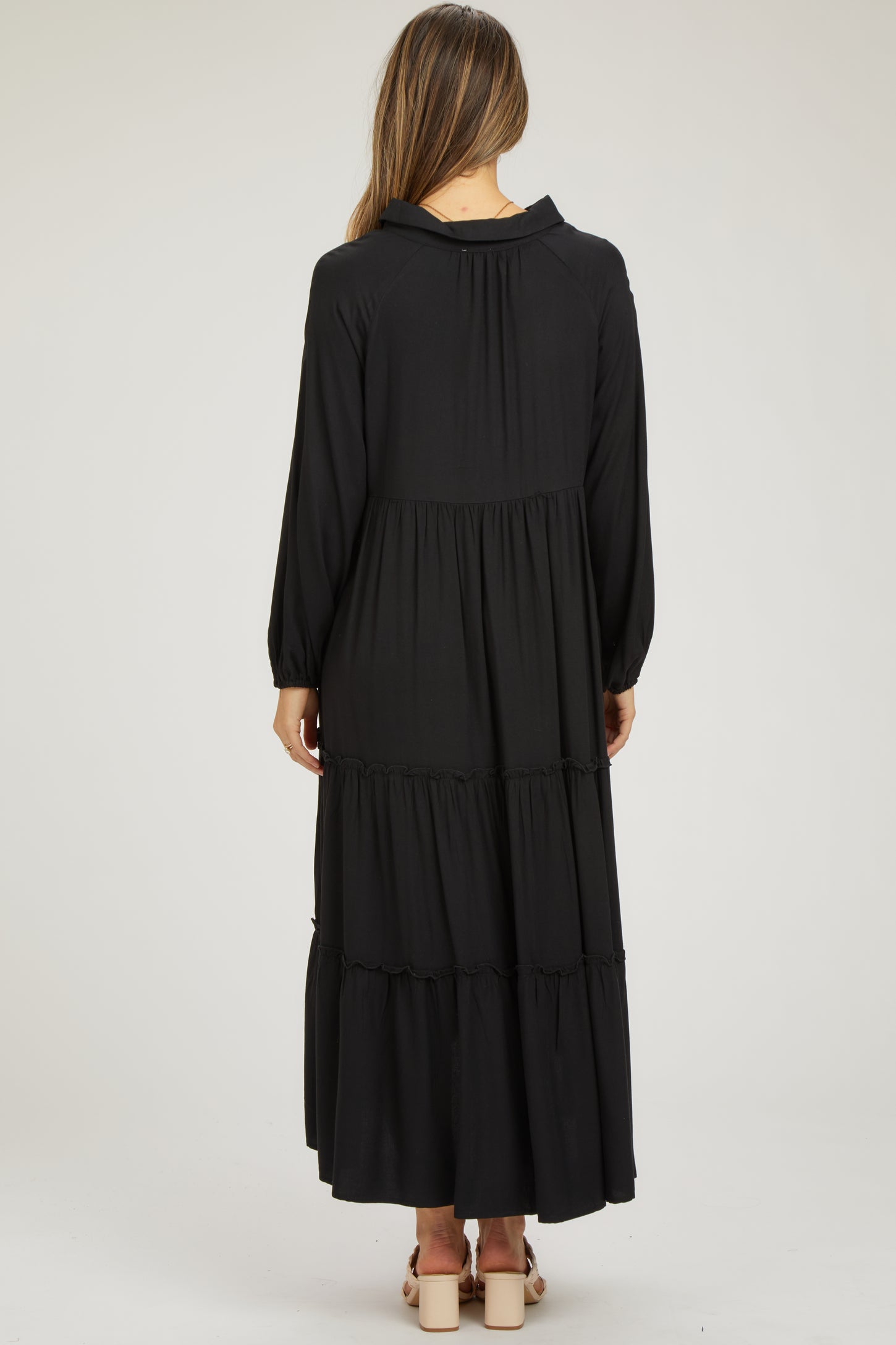 woman wearing a black maternity maxi dress with long sleeves and tiered ruffle details, showing a baby bump from behind