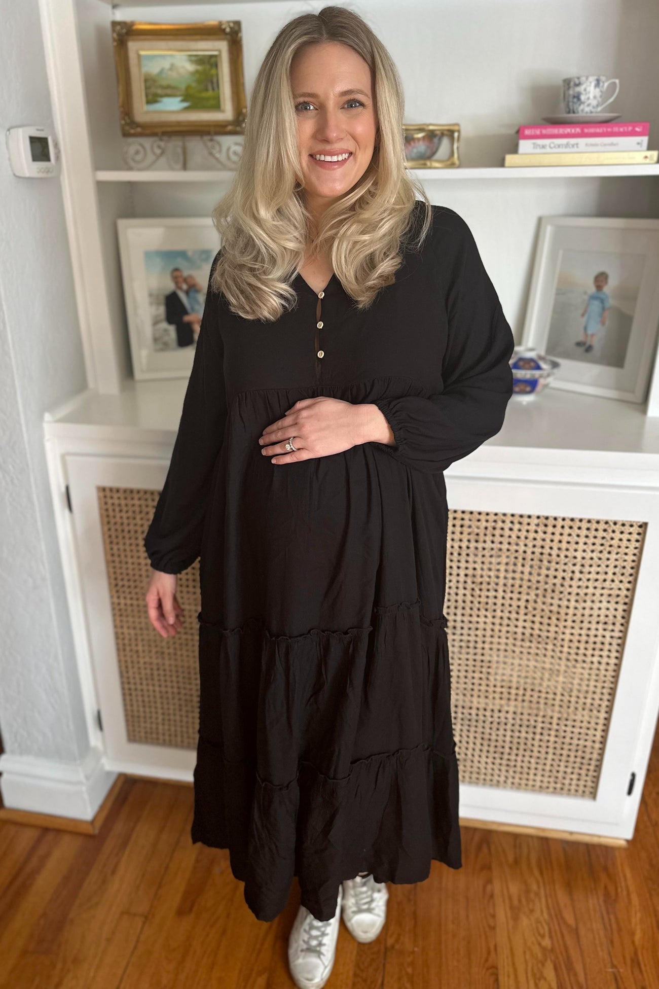 woman wearing a black maternity dress with a tiered design and button details, holding her baby bump