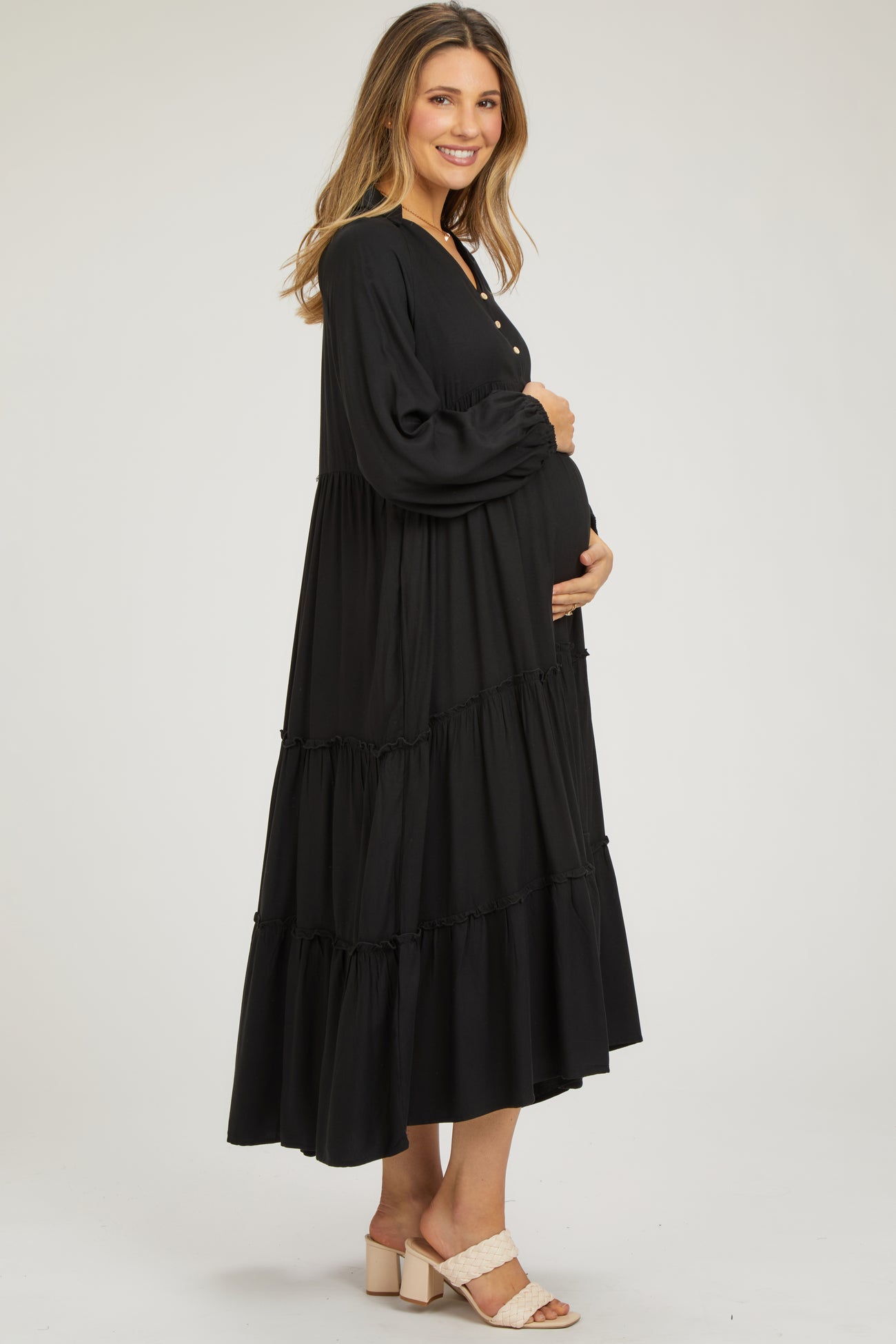 woman wearing a black tiered maxi maternity dress and holding her baby bump