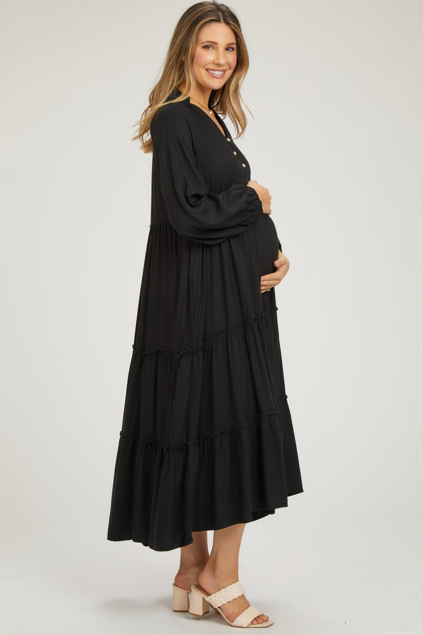 woman wearing a black tiered maxi maternity dress and holding her baby bump