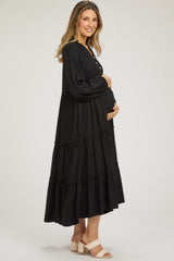 woman wearing a black tiered maxi maternity dress and holding her baby bump