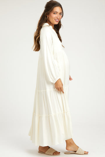woman wearing a white maternity maxi dress with long sleeves and tiered details, showing her baby bump