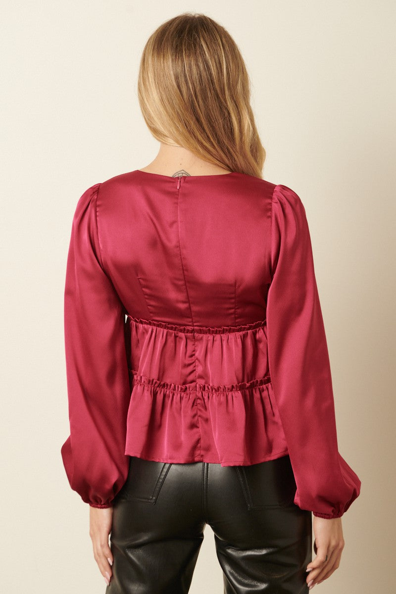 woman wearing a burgundy satin peplum top with long puff sleeves and a cinched waist, shown from the back
