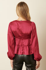 woman wearing a burgundy satin peplum top with long puff sleeves and a cinched waist, shown from the back