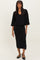 woman wearing a black knit two-piece set with a v-neckline and a midi skirt, standing with a relaxed pose