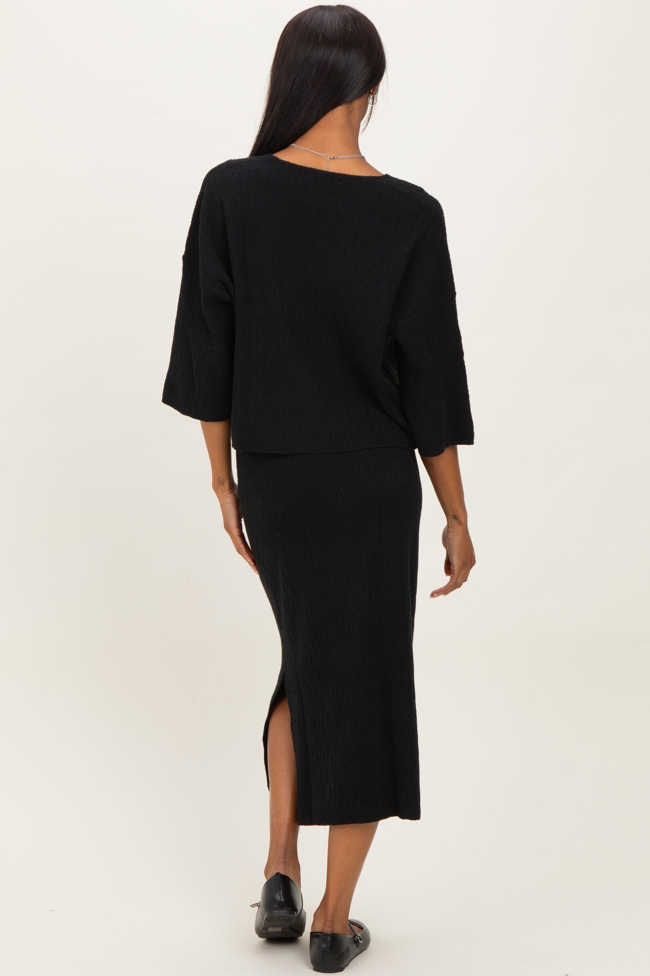 woman wearing a black ribbed two-piece set with a cropped top and midi skirt featuring a side slit