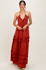 woman wearing a rust red maxi dress with ruffle details and a halter neck design