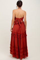 woman wearing a rust-colored maxi dress with a halter neck and ruffled hem, showcasing an open back and tie detail