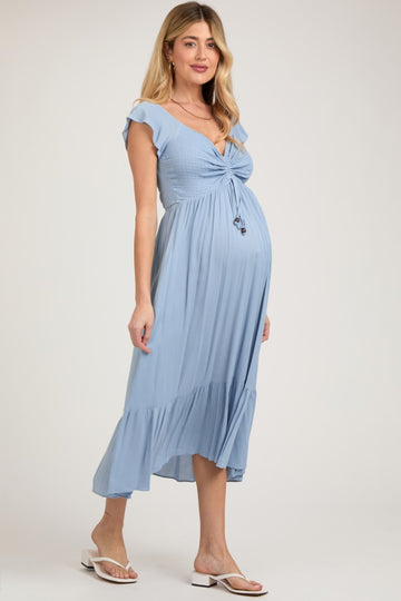woman wearing a light blue maternity dress with a smocked bodice, flutter sleeves, and a flowy skirt, showing a baby bump