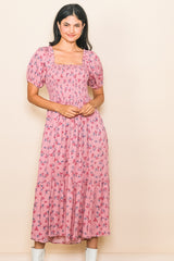 woman wearing a pink floral maxi dress with smocked bodice and puff sleeves, standing against a light background