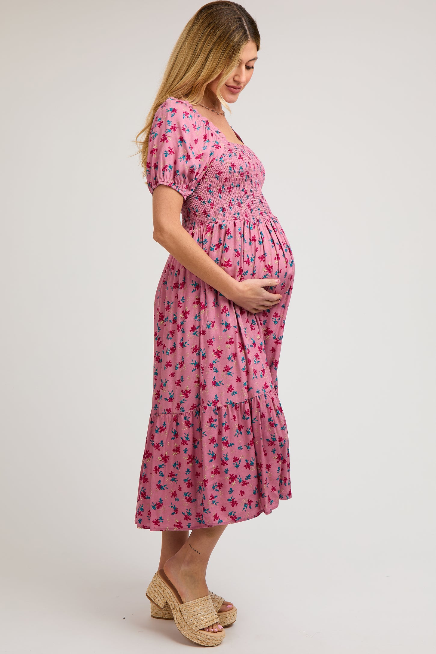 woman wearing a pink floral smocked maternity dress and holding her baby bump
