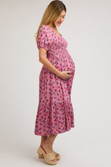 woman wearing a pink floral smocked maternity dress and holding her baby bump