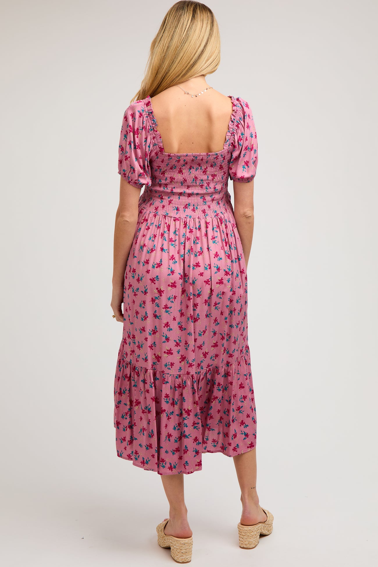 woman wearing a floral pink maternity midi dress with a smocked bodice and puff sleeves, showing her back