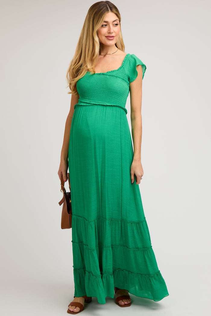 woman wearing a green maternity maxi dress with short flutter sleeves and tiered hem, showcasing her baby bump