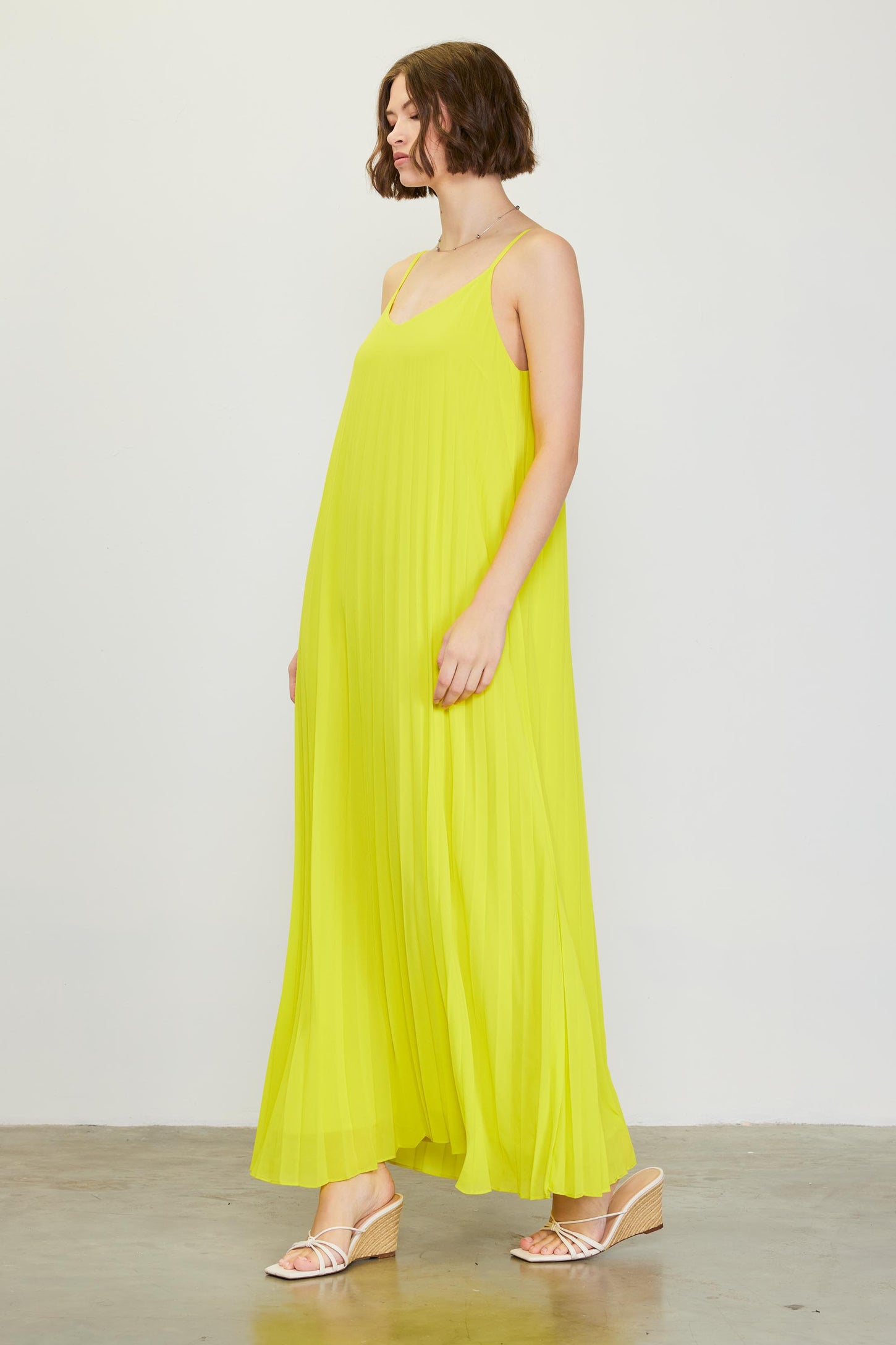 woman wearing a bright yellow pleated maxi dress with spaghetti straps and strappy sandals