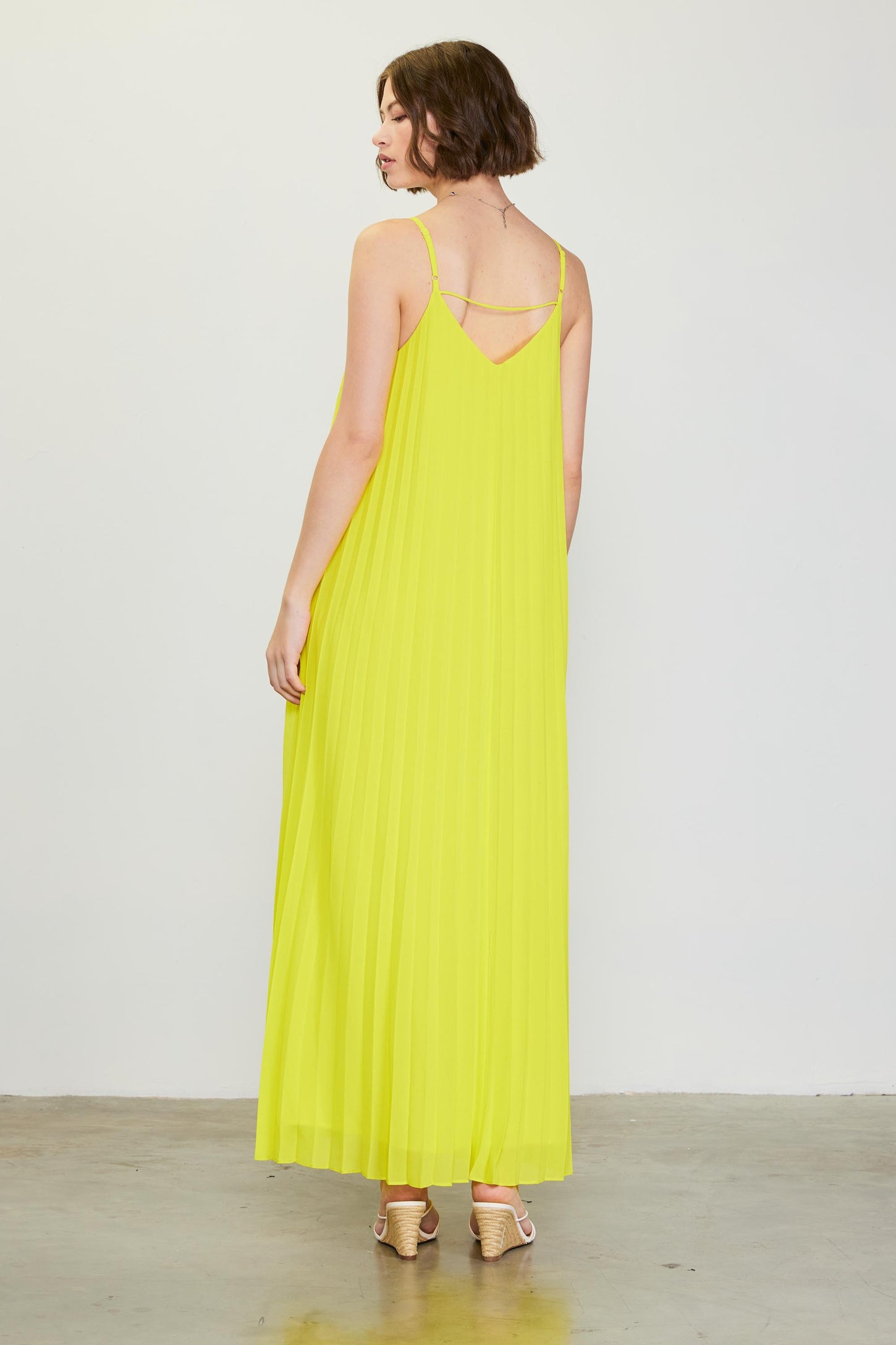 woman wearing a bright yellow pleated maxi dress with spaghetti straps and a V-back design