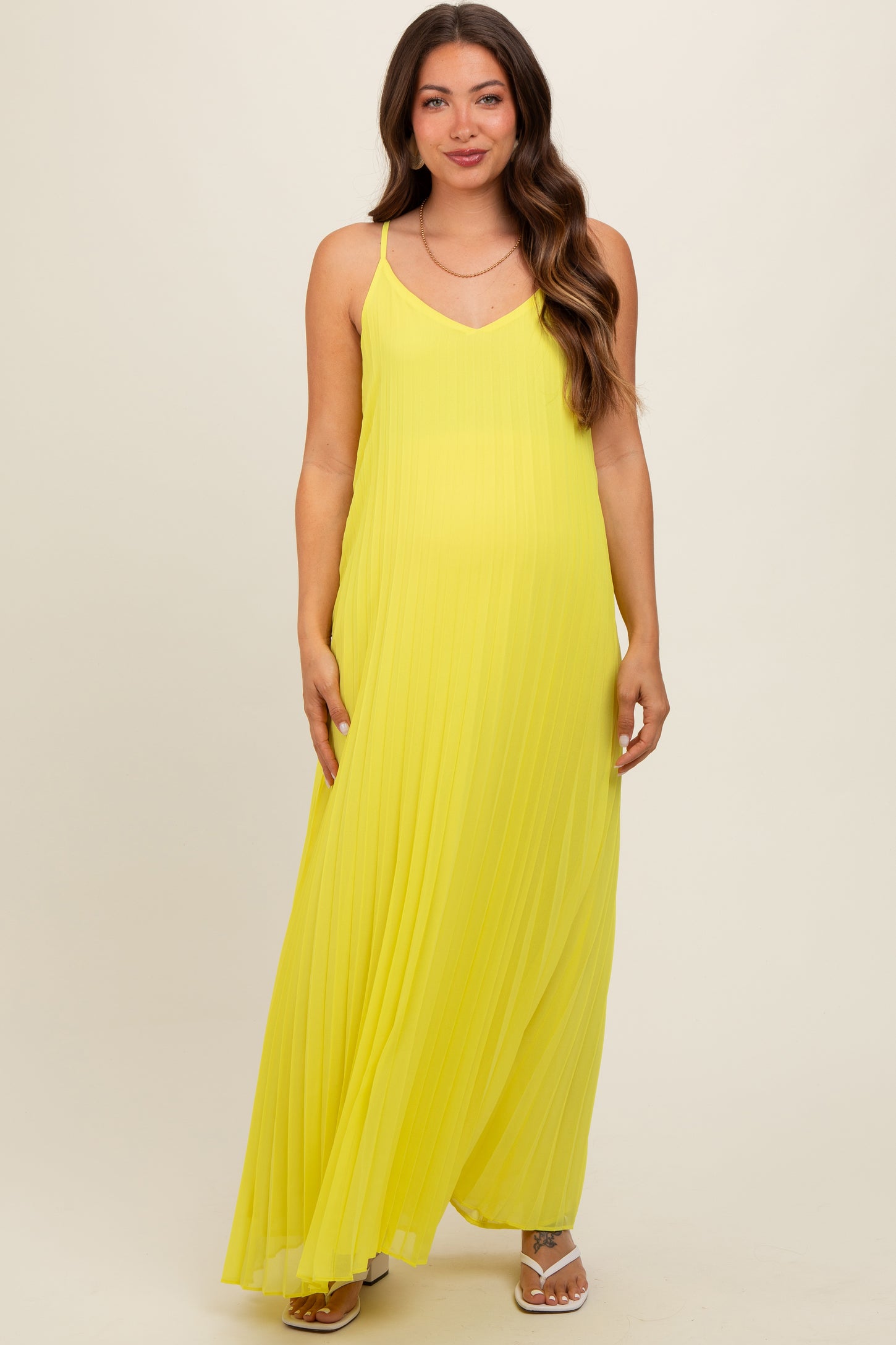 woman wearing a bright yellow pleated maternity maxi dress with spaghetti straps and a flowing silhouette